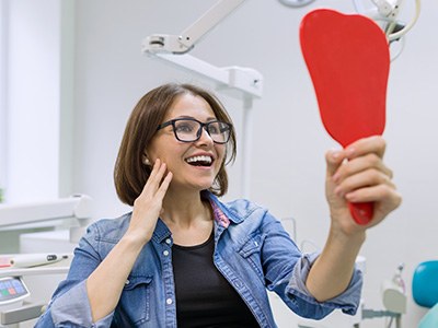 A woman using a hand mirror to admire her new dental implant