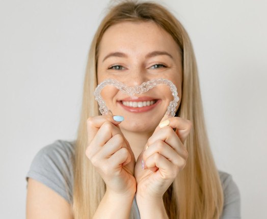 A smiling woman holding two Invisalign trays to look like a heart