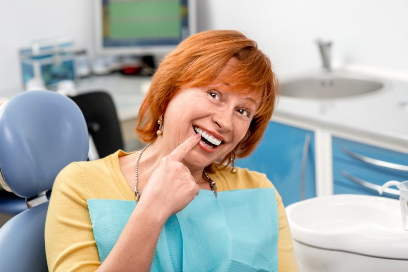 A happy senior woman pointing to the new dental implants in her mouth